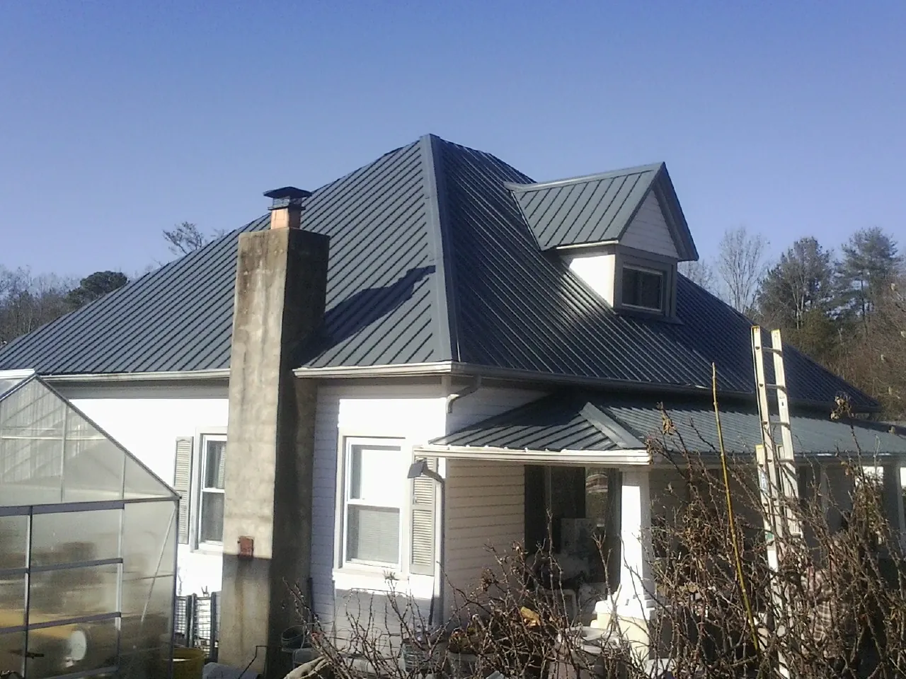Dark blue standing seam metal roof on a white farmhouse with dormer in Concord